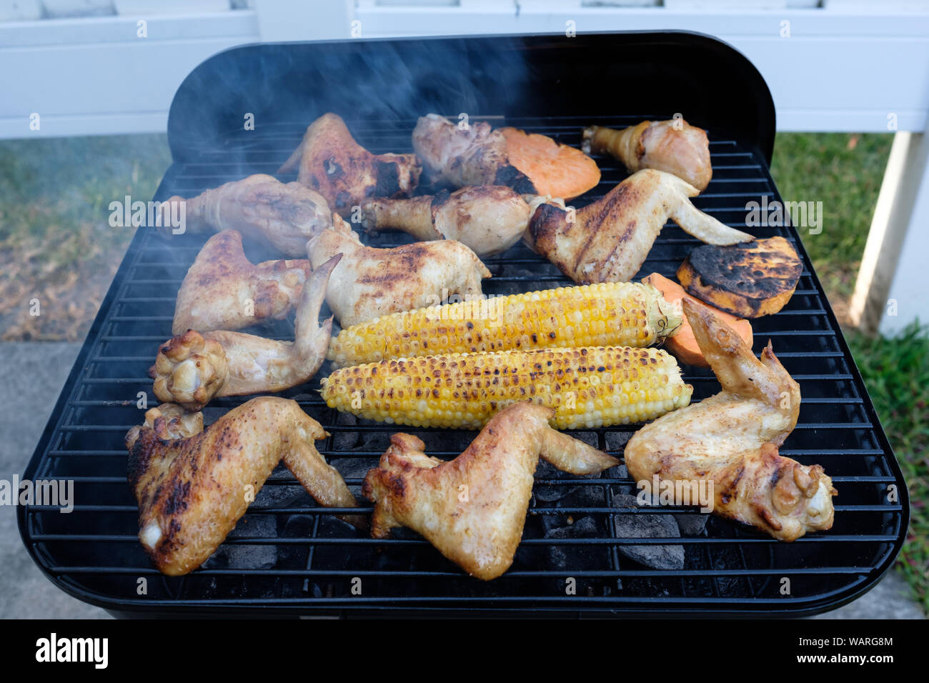 Estate barbecue per la cottura su un fuoco caldo con ali di pollo, bacchette e mais Foto Stock
