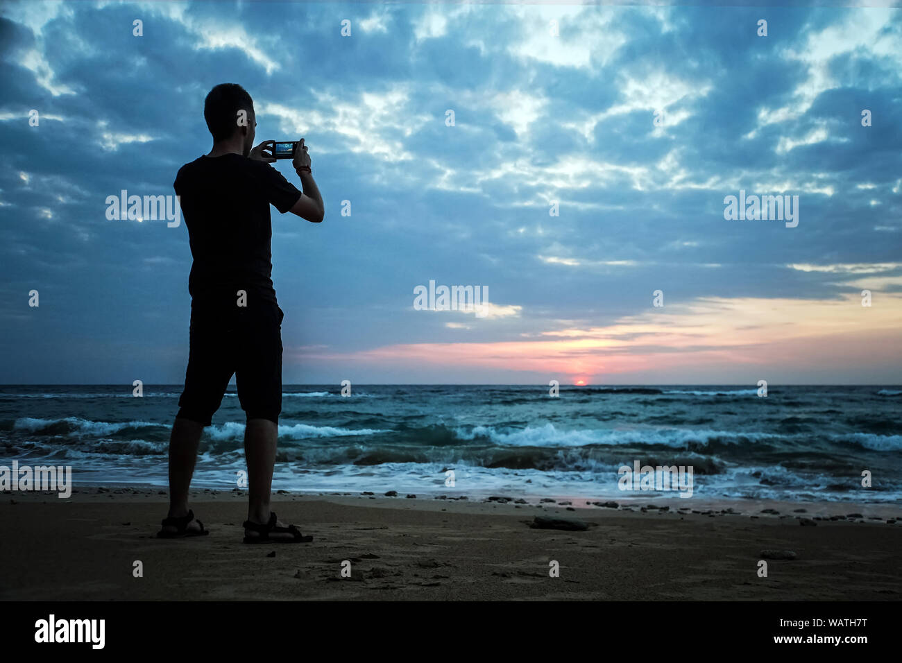 Smart phone artista fotografia sul corrimano sulla mole Sun al di sopra del mare di mattina orizzonte. Tourist guarda il sole al di sopra di buon livello oceano Foto Stock