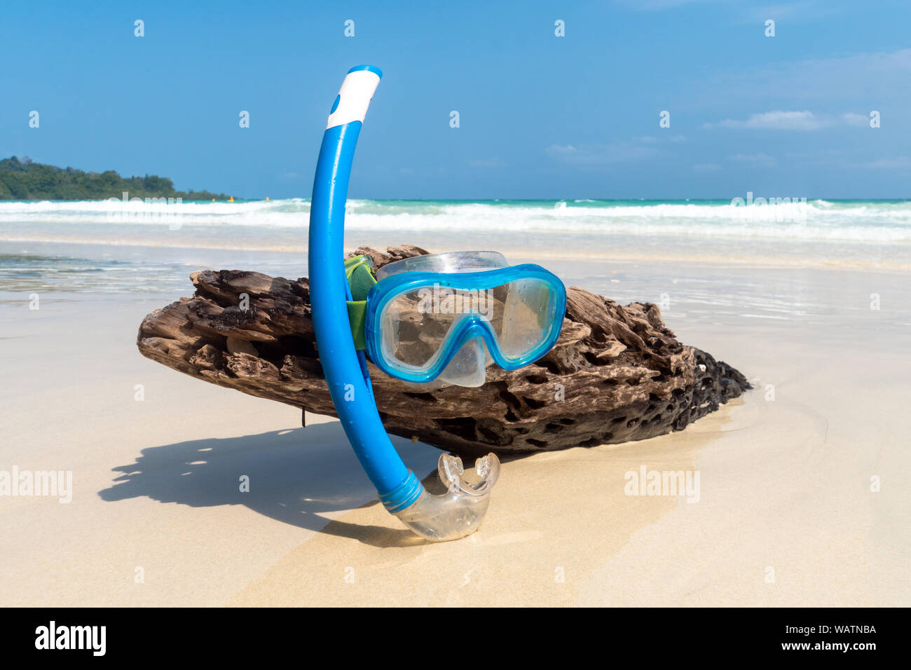 Lo snorkeling maschera sull'albero secco umido con bel mare blu e isola nella giornata di sole dell'estate. Attrezzatura snorkeling su un tronco di legno fuori del th Foto Stock
