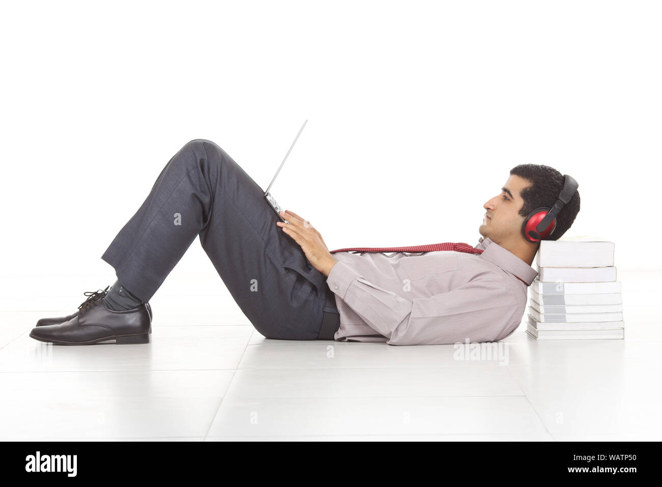 Uomo d'affari che si trova contro una pila di libri e l'uso di computer portatile con ascoltare musica Foto Stock