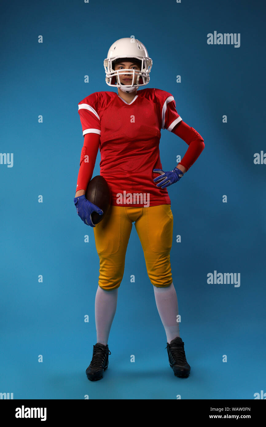 A tutta lunghezza foto di giovane donna americana giocatore di football nel casco bianco, sportswear con la palla in mano isolato in bianco su sfondo blu Foto Stock