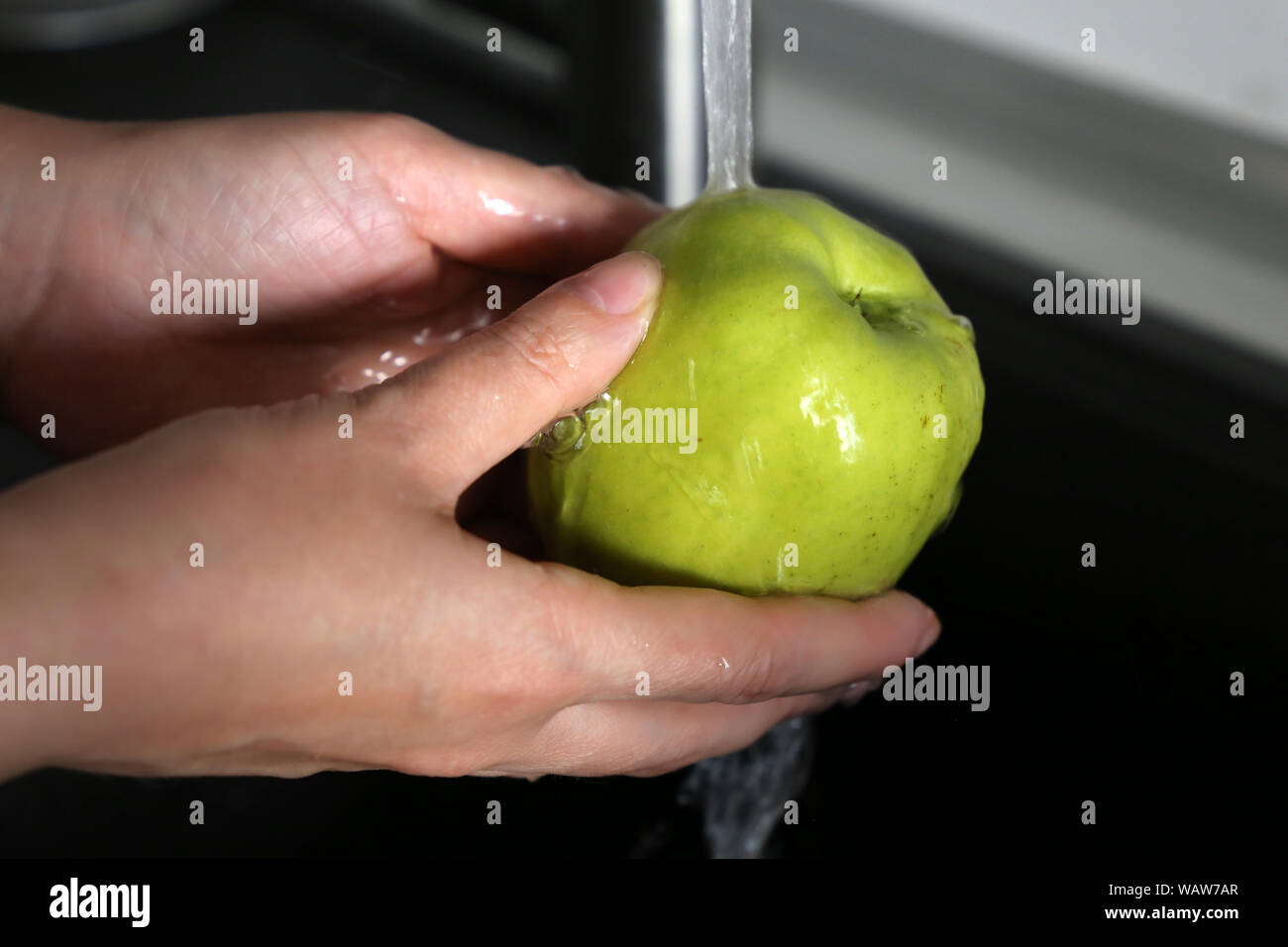 La donna lava una mela verde sotto acqua di rubinetto. Concetto di igiene, pulire la frutta in mani femminili Foto Stock