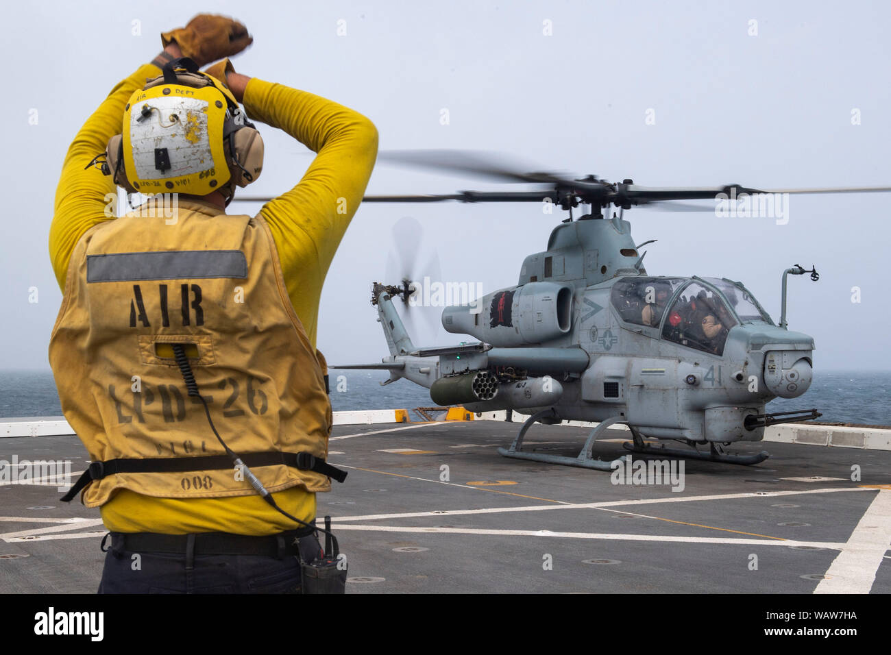 190815-N-NB544-1046 Golfo di Aden (Agosto 15, 2019) di aviazione di Boatswain Mate (movimentazione) terza classe James Ling, segnali di AH-1Z Viper piloti, assegnato a mezzo marino Tiltrotor Squadron (VMM) 163 (rinforzato), durante le operazioni di volo a bordo del trasporto anfibio dock nave USS John P. Murtha (LPD 26). John P. Murtha parte del Boxer anfibio gruppo pronto e undicesimo Marine Expeditionary Unit ed è distribuito negli Stati Uniti Quinta Flotta area di operazioni a sostegno di operazioni navali per garantire stabilità marittimo e la sicurezza nella regione centrale di collegamento del Mediterraneo e del Pacifico attraverso Foto Stock