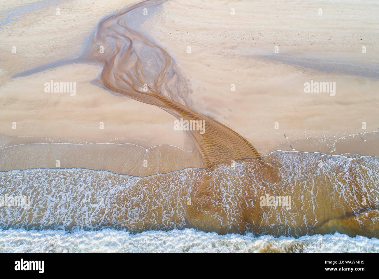 Creek con rossastro acqua ferruginosa scorre su di una spiaggia di sabbia nel mare, vicino a Stornoway, isola di Lewis e Harris Isola, Scozia, Gran Bretagna. Foto Stock