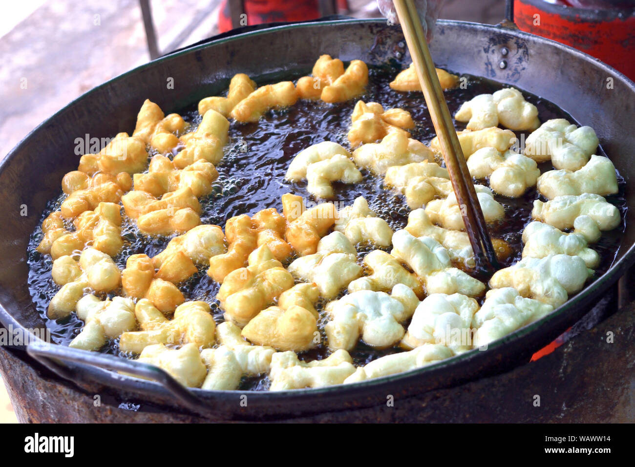 Fritte doughstick fluttuante nel caldo di olio di cottura, bastoncini sono la cattura di alimenti fritti flipping avanti e indietro in padella Foto Stock