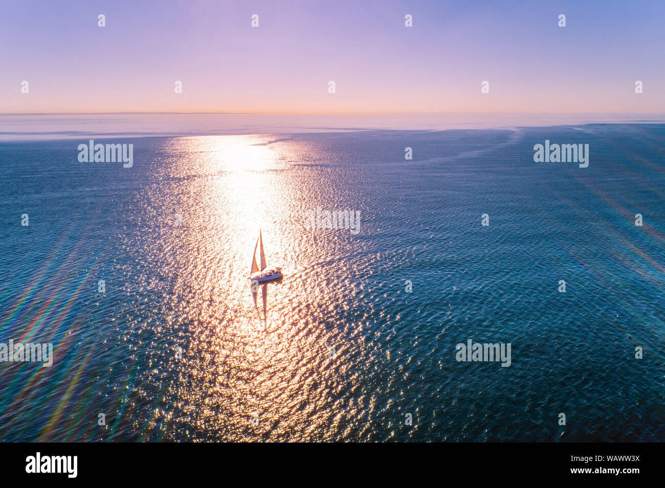 Barca a vela in oceano con forte retroilluminazione al tramonto - antenna minimalista seascape con spazio di copia Foto Stock