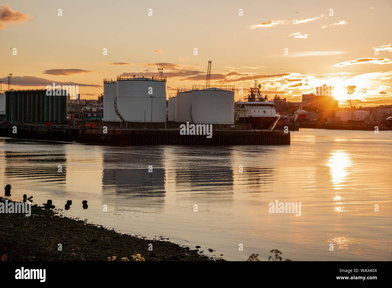 Serbatoi di olio su un molo in un porto commerciale al tramonto Foto Stock