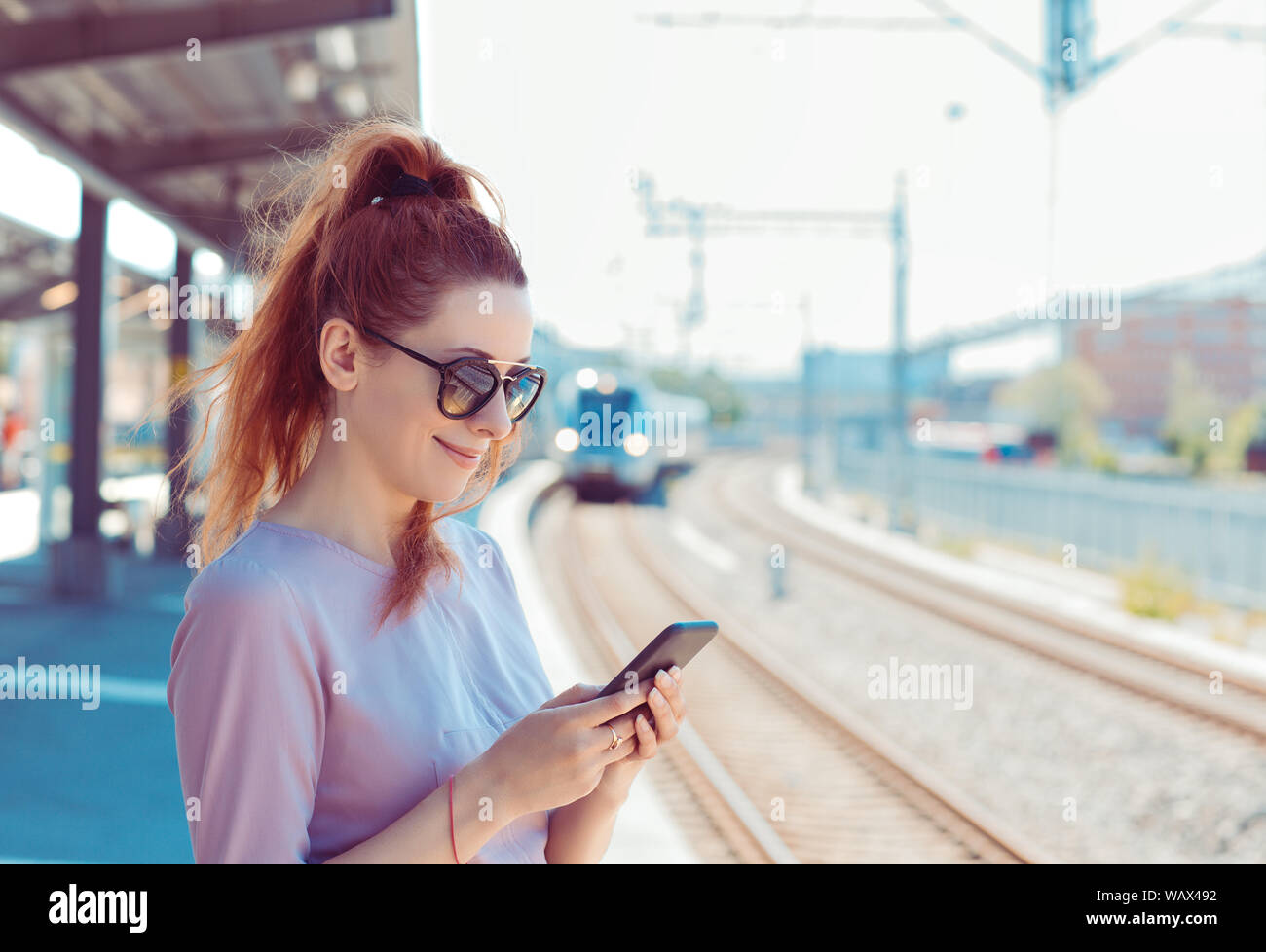 Giovane donna con il suo telefono cellulare sulla piattaforma della metropolitana, controllo messaggi sms e-mail o orari dei treni. Ragazza texting sullo smartphone mentre il treno cittadino approa Foto Stock