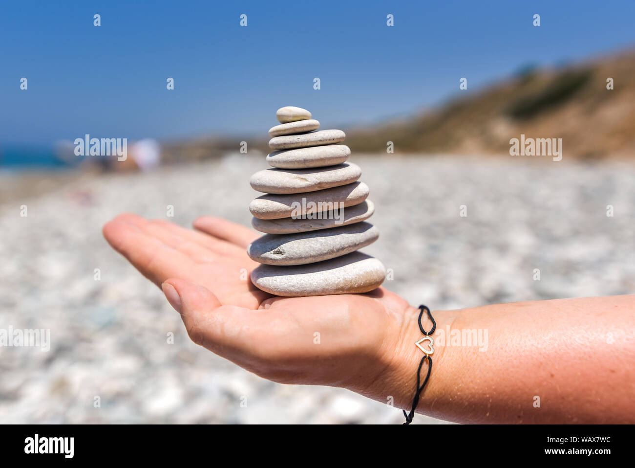 Una pila di meditazione spiaggia spiaggia di roccia essendo tenuto con cura da una donna mano Foto Stock
