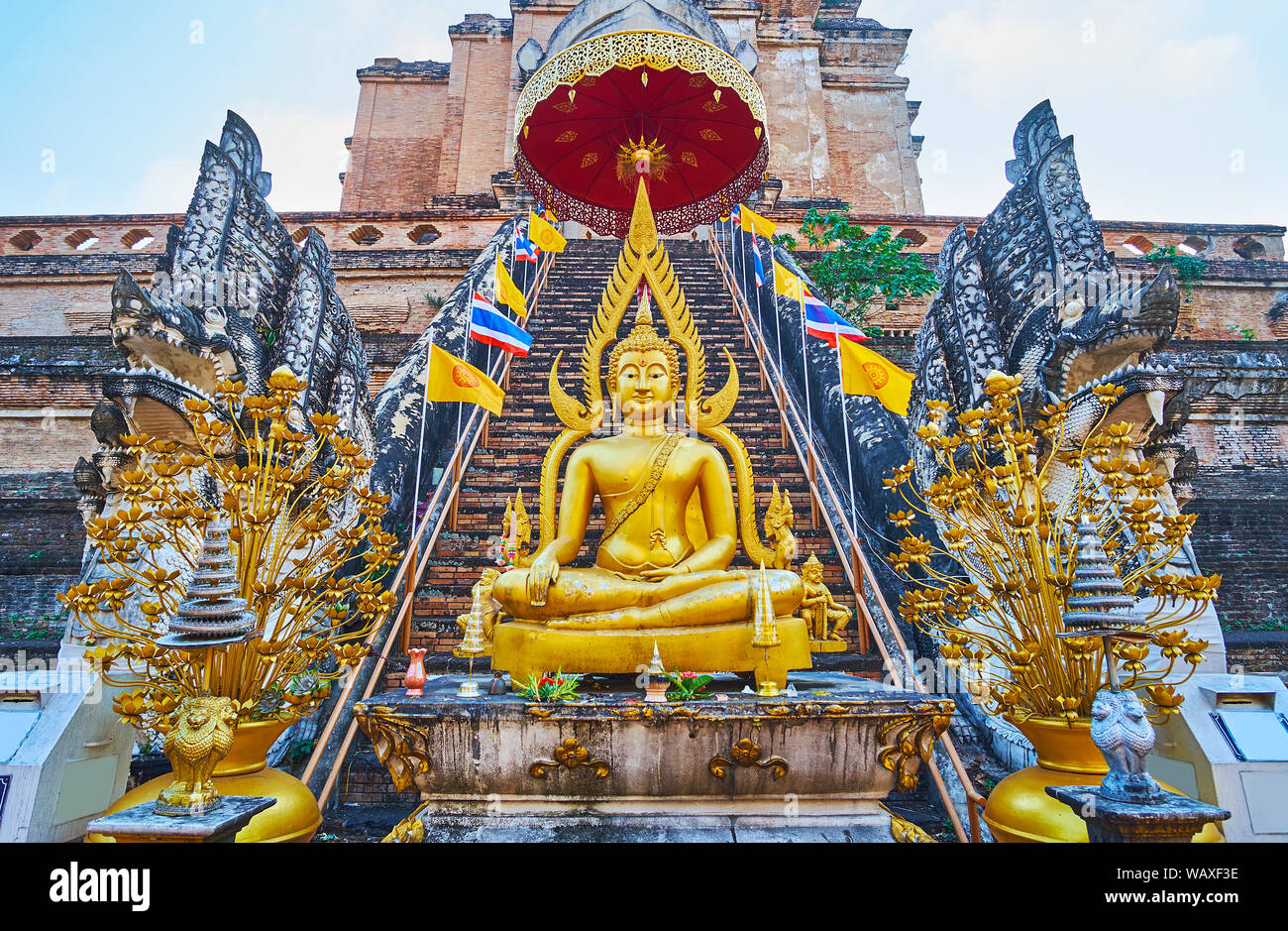 Il golden immagine del Buddha con chatra ombrello cerimoniale, dorate vasi con fiori e pietra scolpita Naga serpenti di Phra Chedi Luang, Wat Chedi Luan Foto Stock