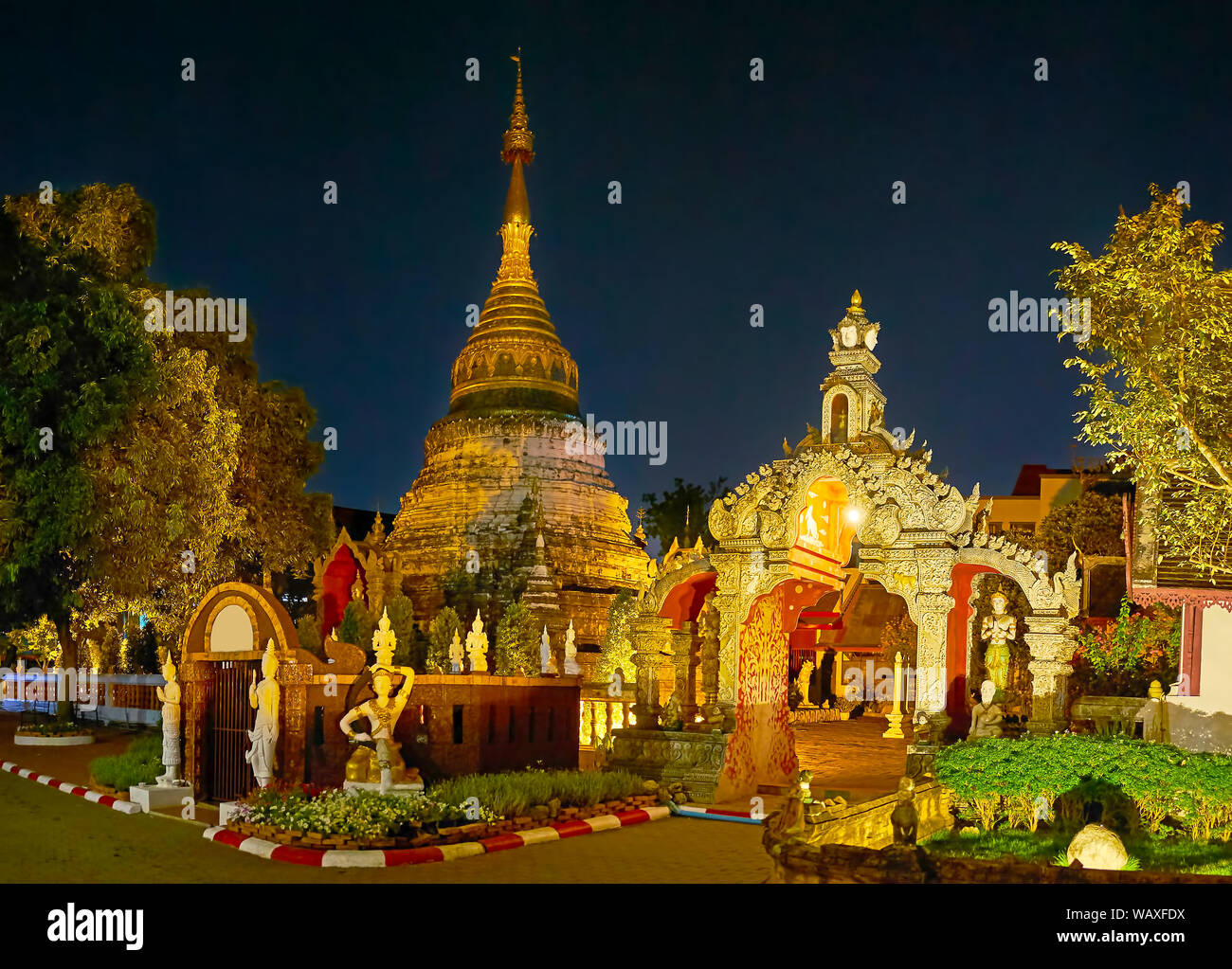 A piedi la sera il giardino di Wat Mahawanand godetevi la vista sulla sua scolpiti chedi, situato dietro gli intricati gate in stucco, Chiang Mai, Thailandia Foto Stock