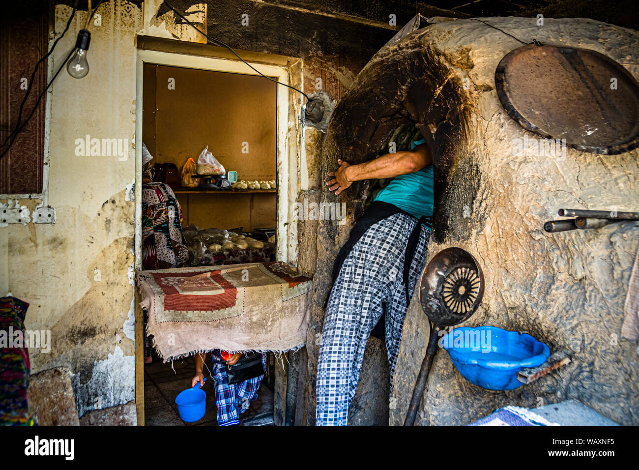 Un fornaio si china profondamente nel forno tandoor per premere un pezzo di impasto contro la sua parete interna calda, Osh, Kirghizistan. Foto Stock
