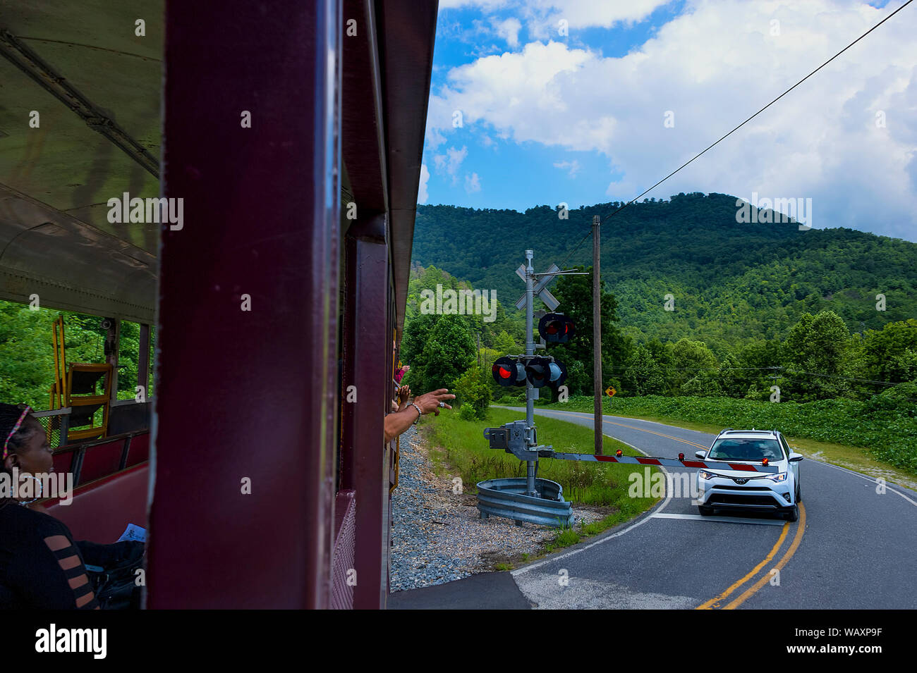 Bryson, North Carolina, Stati Uniti d'America - 3 Agosto 2019: turistici su una vista vedere treno wave a un automobilista si è fermato a un attraversamento ferroviario. Foto Stock