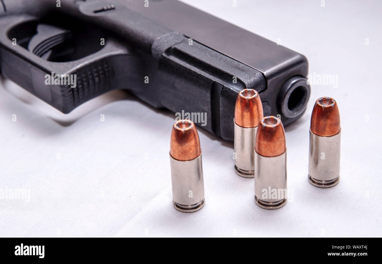 Un nero 9mm pistola con quattro punti di cava pallottole di fronte ad esso su sfondo bianco Foto Stock
