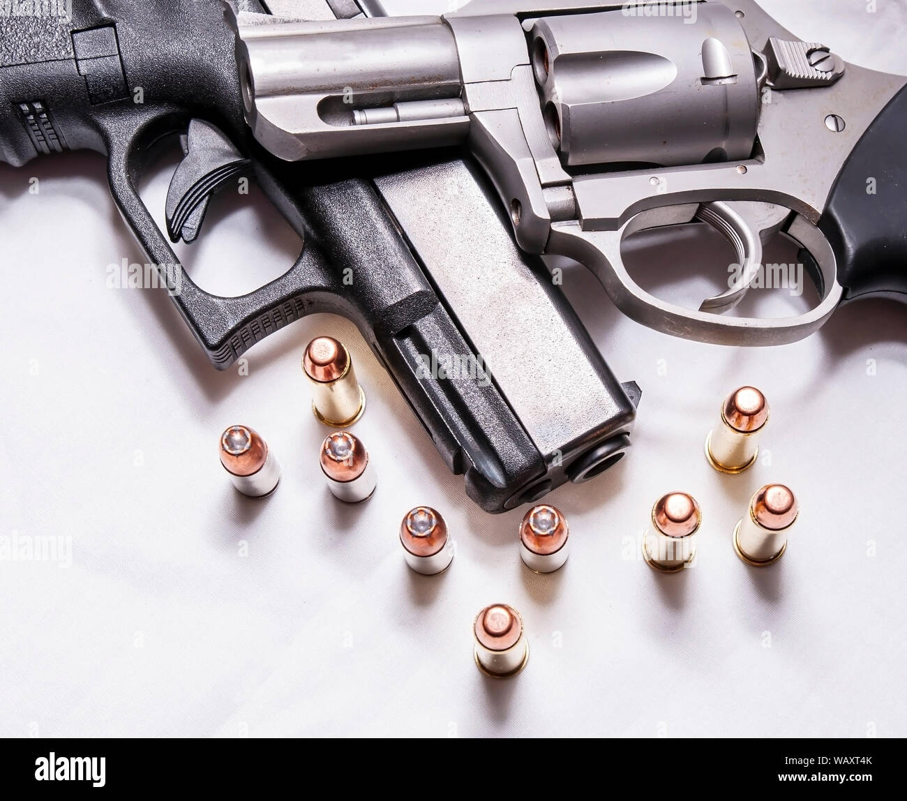 Un naso camuso, acciaio inossidabile 357 revolver Magnum sulla parte superiore di un nero 9mm pistola con alcuni proiettili per ogni calibro di fronte a loro su uno sfondo bianco Foto Stock