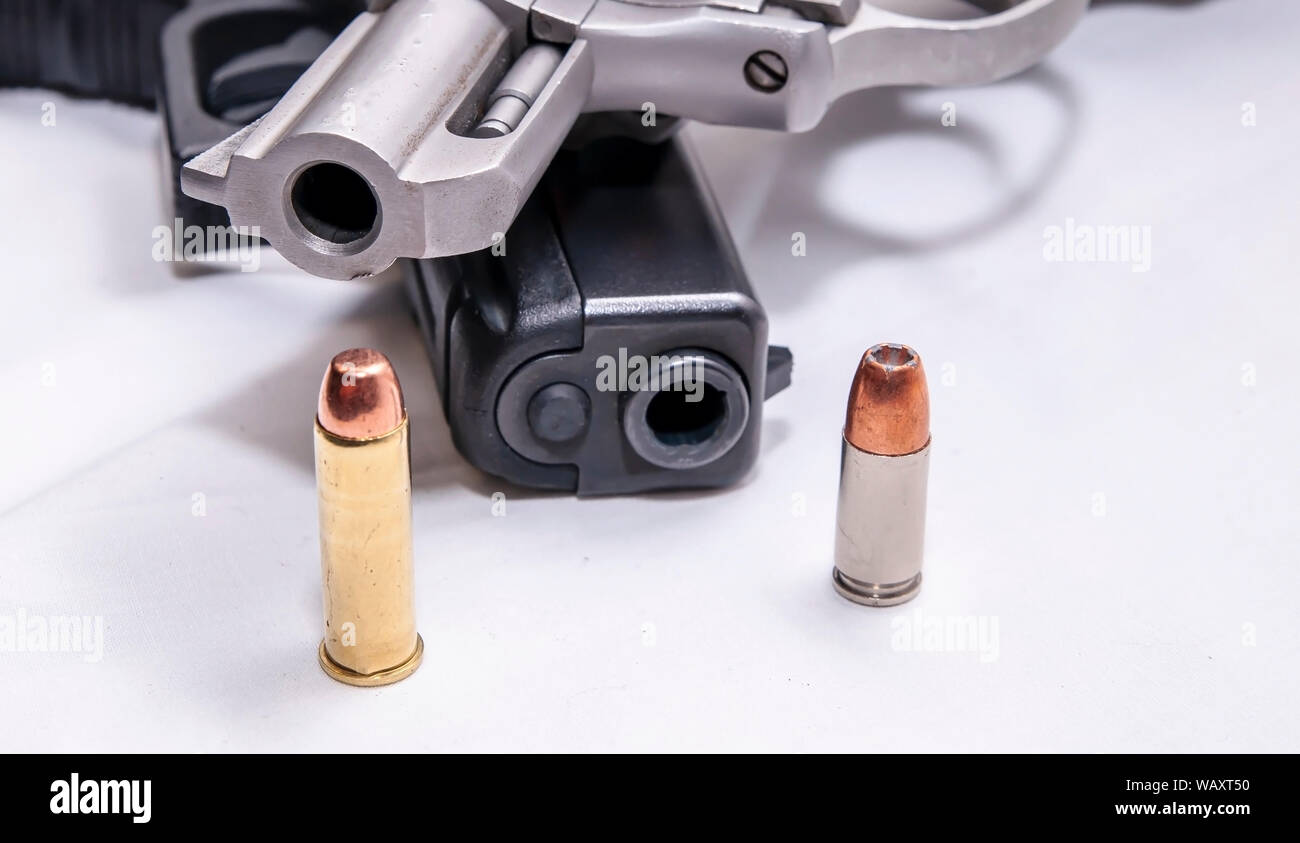 Un naso camuso, acciaio inossidabile 357 revolver Magnum sulla parte superiore di un nero 9mm pistola con un proiettile per ogni calibro di fronte a loro su uno sfondo bianco Foto Stock