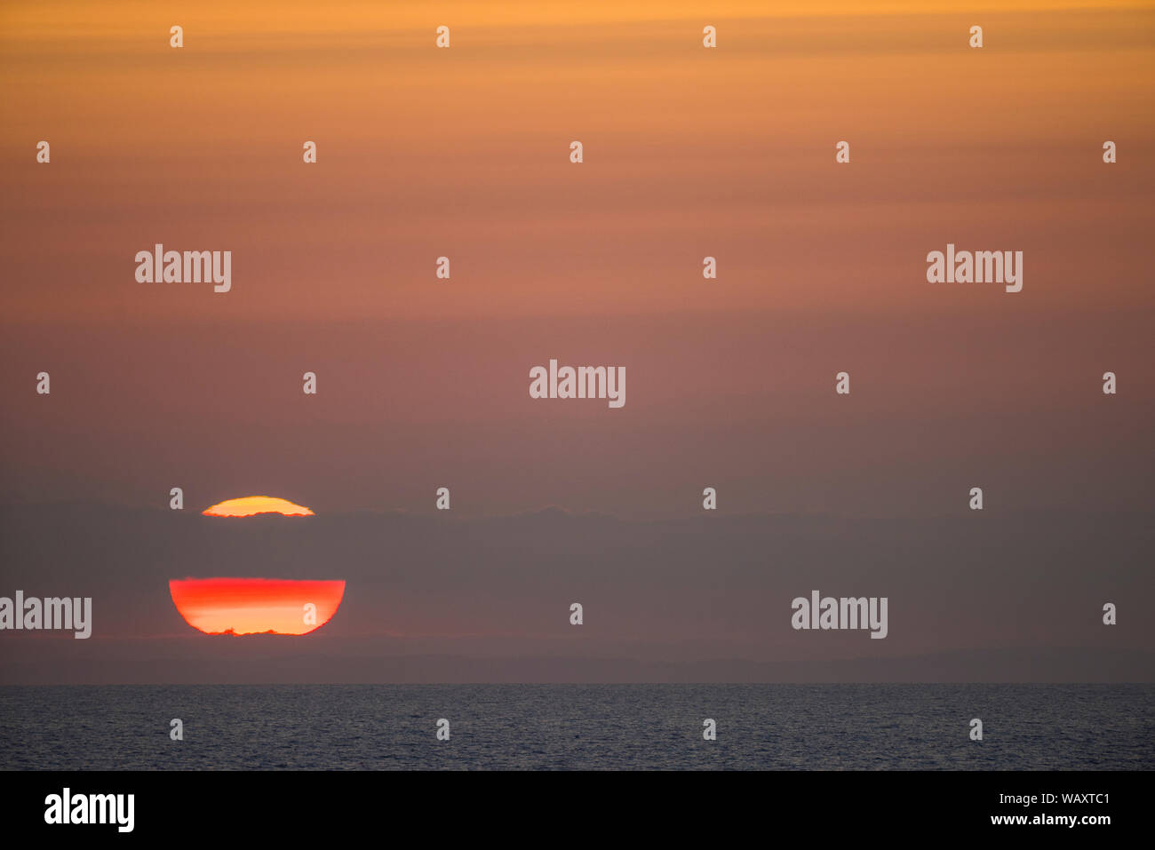 Moody tramonto sul mare con banda di cloud che copra una parte del sun. Foto Stock