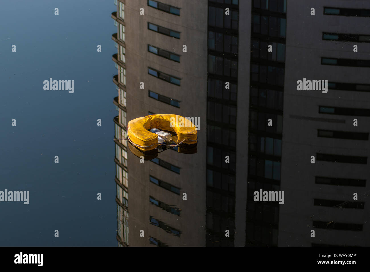 Ferro di Cavallo giallo salvagente e bottiglie di plastica galleggiante sull'acqua con la riflessione di un edificio. Foto Stock