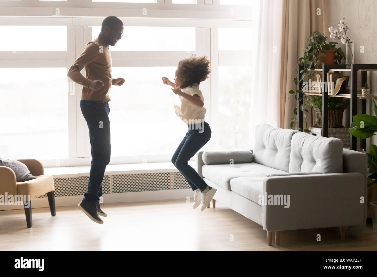 Felice americano africano padre e figlia piccola jumping insieme Foto Stock