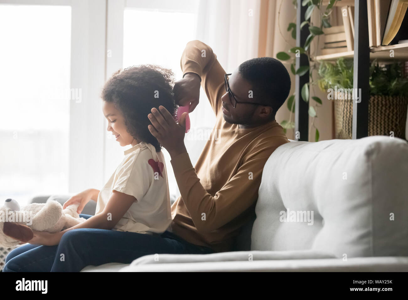 Caring americano africano padre di spazzolatura in età prescolare di pettinatura dei capelli figlia Foto Stock