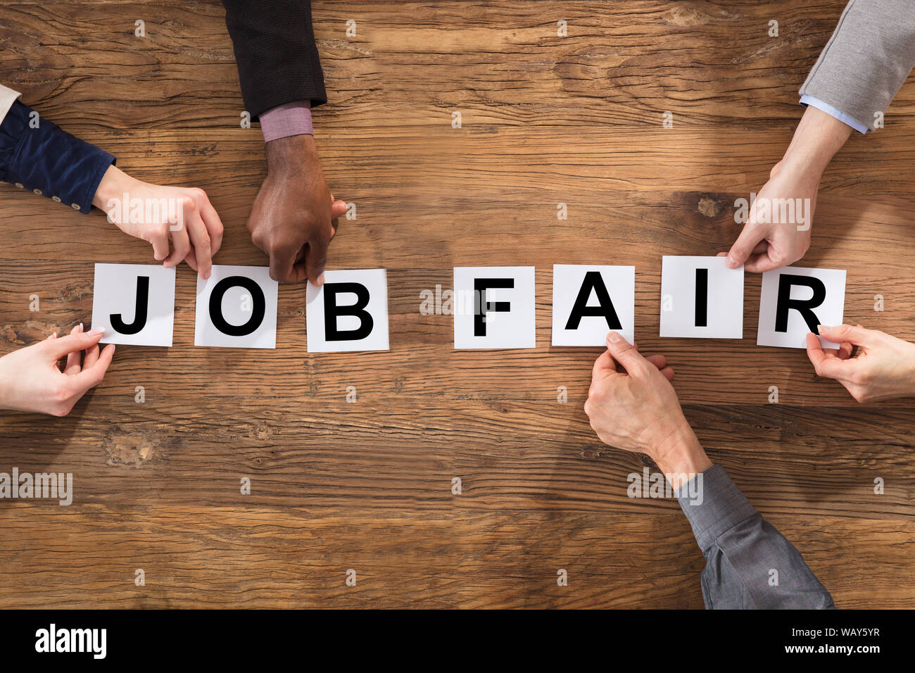Una vista aerea di gente di affari disponendo le mani Job Fair parola sulla scrivania in legno Foto Stock