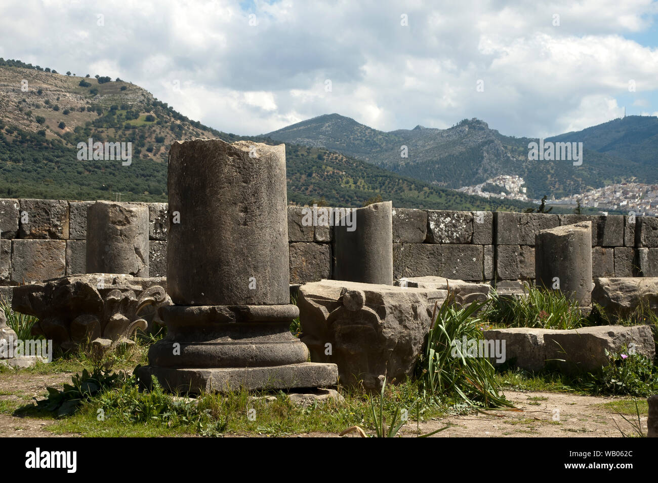 Volubilis Marocco, parziale colonne romane con il villaggio di Moulay Idriss Zerhoun in background Foto Stock