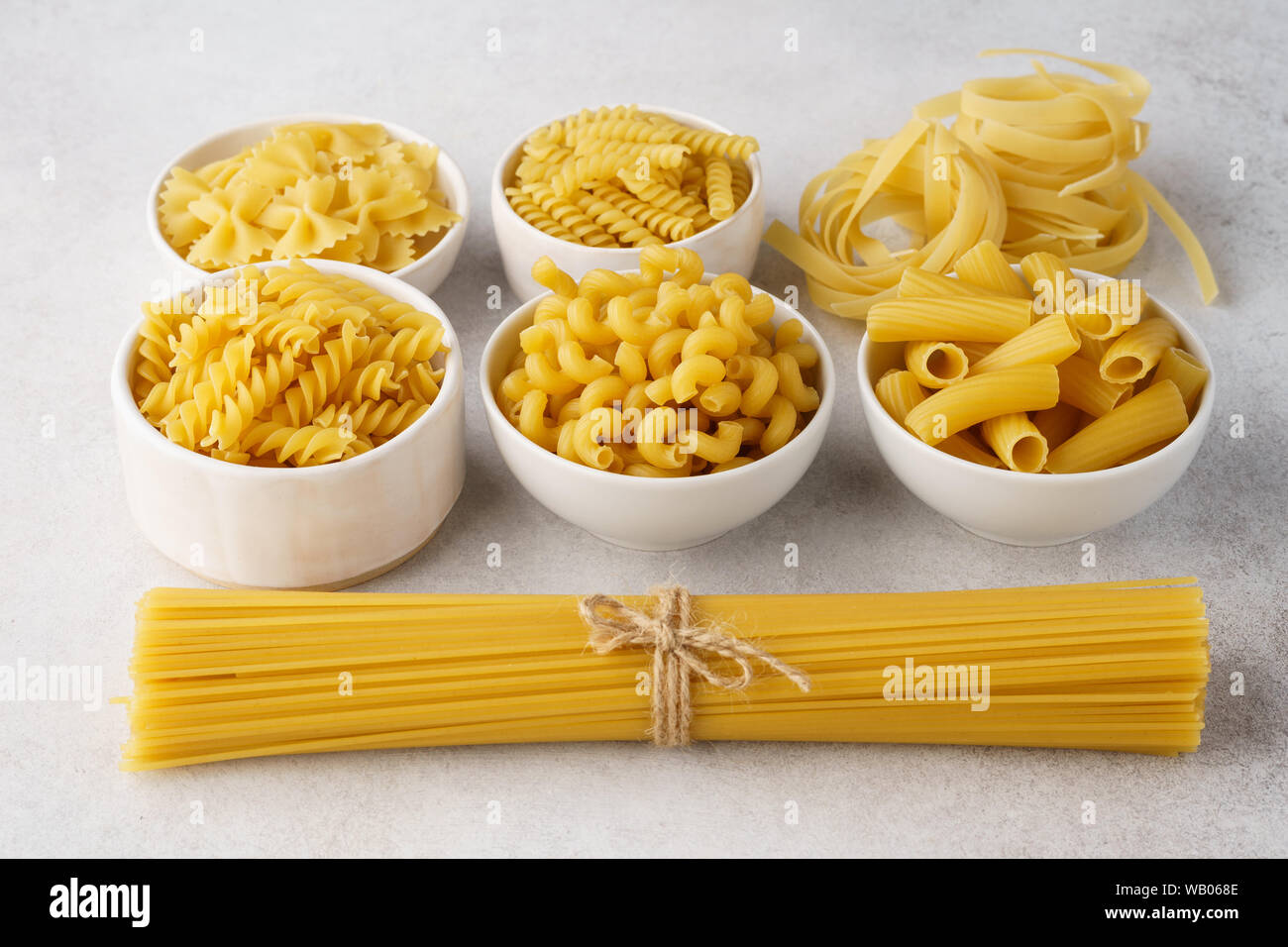 Vari tipi di pasta secca in ciotole su sfondo grigio chiaro. Ingredienti per la cottura. Foto Stock