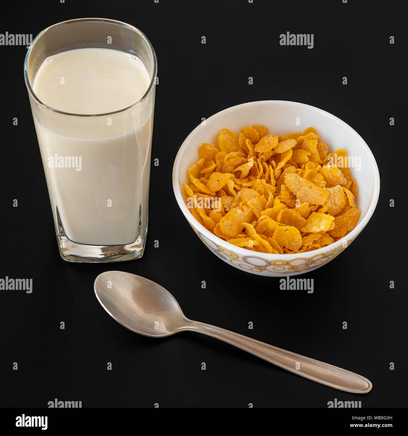 Cornflakes con latte in blowl con latte isolate in vetro nero su sfondo grigio, una deliziosa dietetici di cereali per la prima colazione. Foto Stock