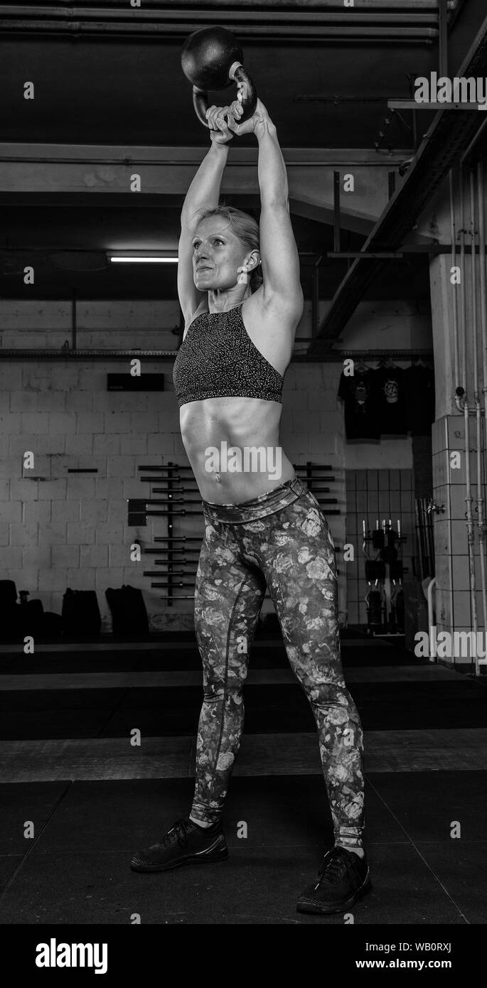 Un attraente donna di mezza età con forte abs sta facendo kettlebell altalene. L'atleta femminile sta facendo un funzionale allenamento fitness in una palestra. Foto Stock