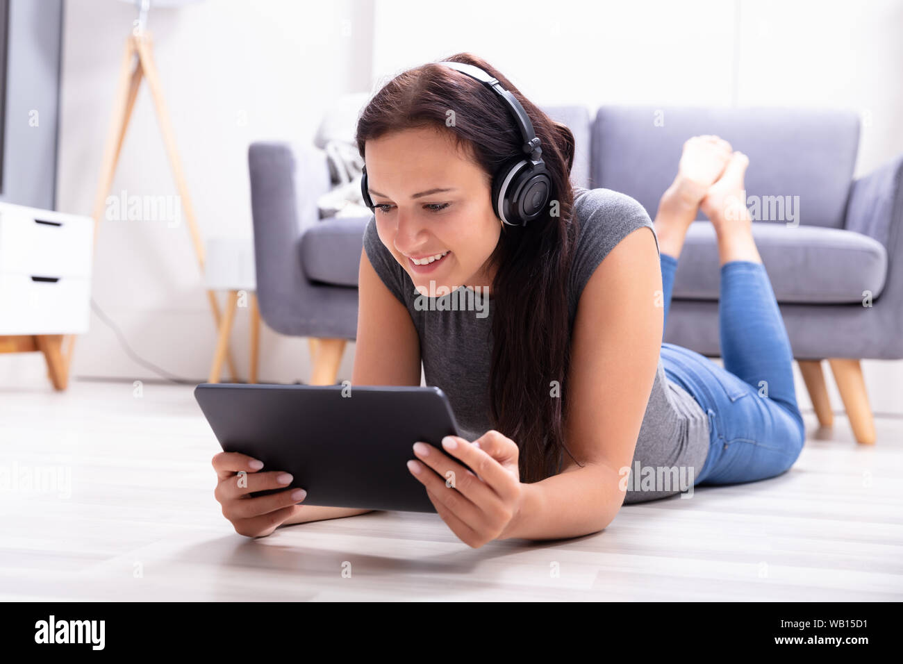 Felice giovane donna sdraiata sul pavimento godendo la musica in cuffia utilizzando tavoletta digitale Foto Stock