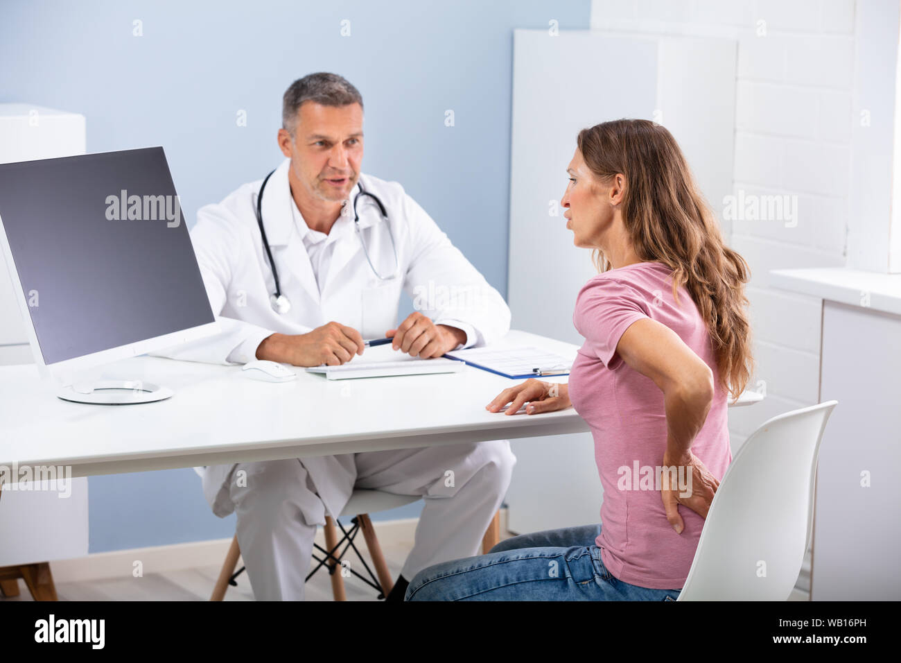 Medico di sesso maschile di parlare con paziente di sesso femminile affetti da mal di schiena in clinica Foto Stock