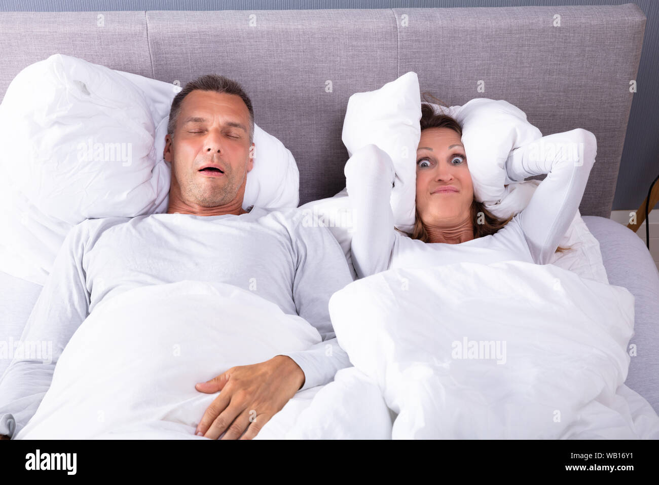 Donna matura che copre le sue orecchie con cuscino durante l uomo il russamento nel letto Foto Stock
