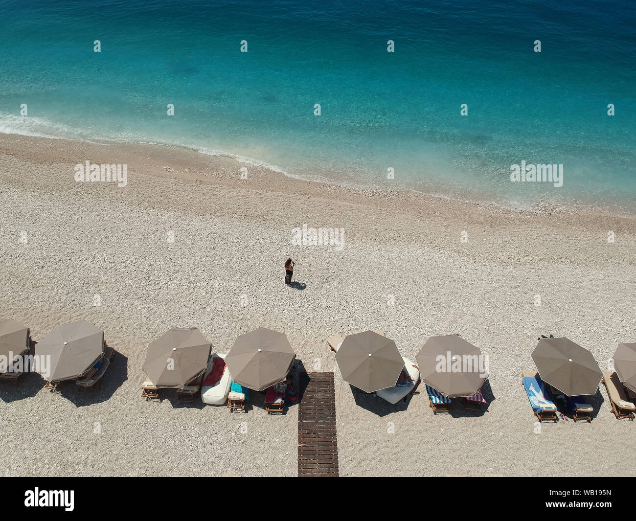 Vista aerea spiaggia rocciosa e crystal acque turchesi del Mar Ionio in Albania. Calma e rilassante vista in Palase spiaggia, ombrelloni e lettini Foto Stock