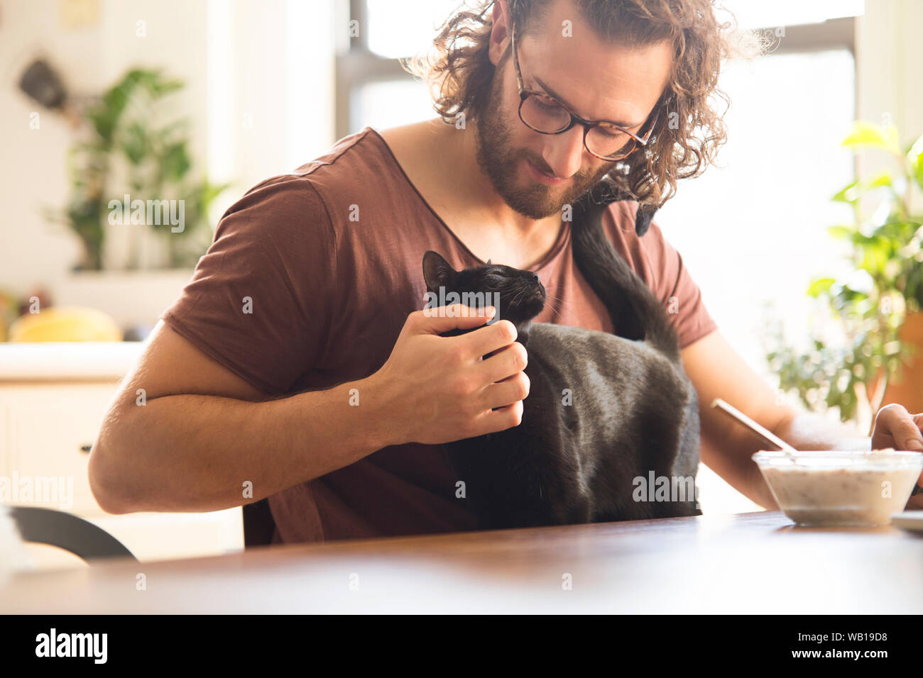 Giovane uomo di accarezzare il suo gatto nero a casa Foto Stock