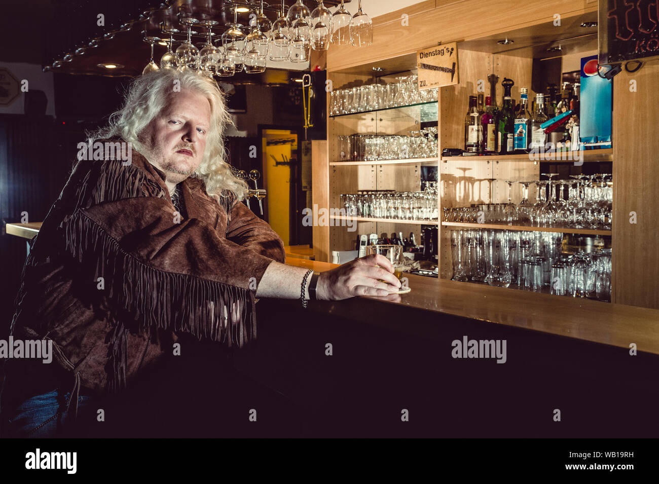 Ritratto di bilanciere bionda indossando giacca di pelle marrone in piedi al bancone di un vecchio pub Foto Stock