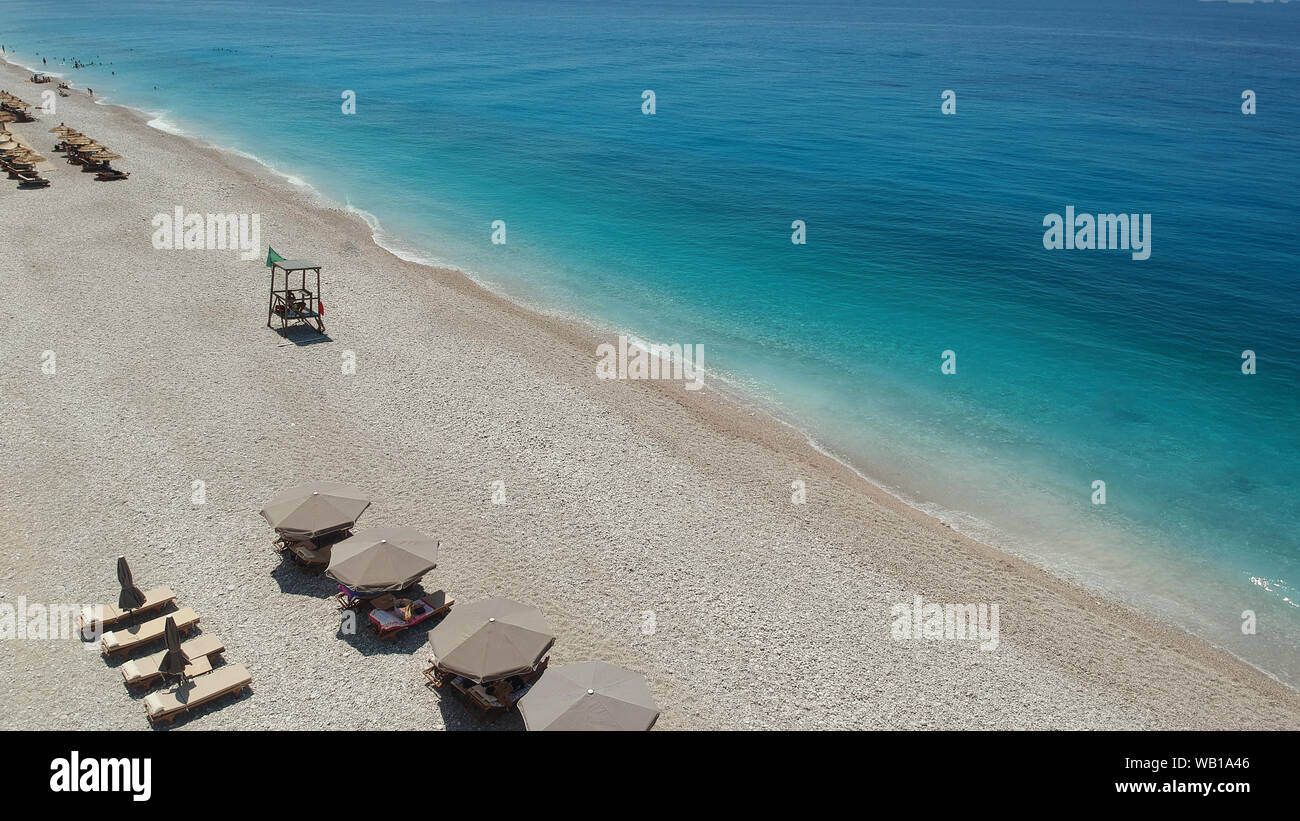 Vista aerea spiaggia rocciosa e crystal acque turchesi del Mar Ionio in Albania. Calma e rilassante vista in Palase spiaggia, ombrelloni e lettini Foto Stock