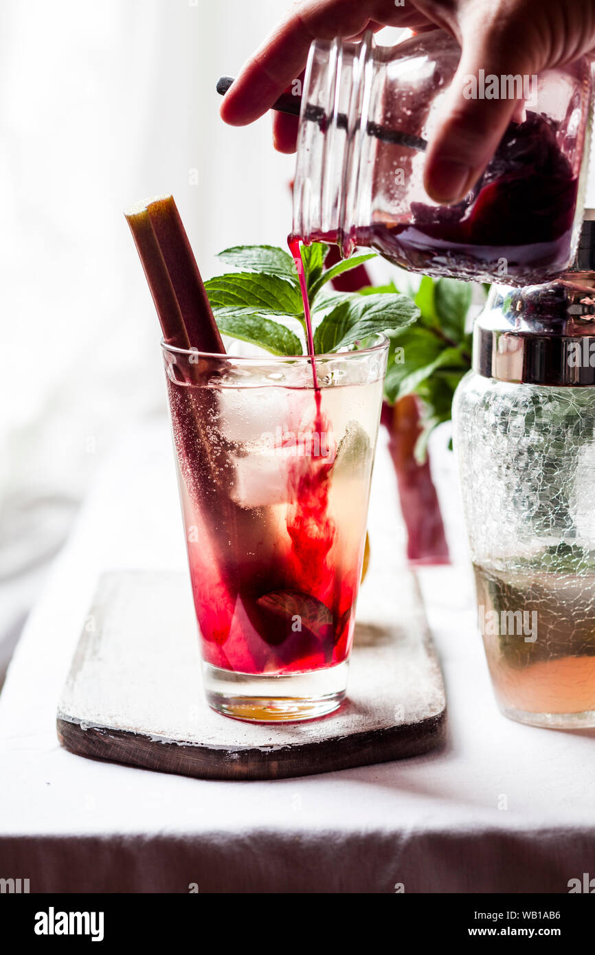 La preparazione di rabarbaro Collins con gin, prosecco, succo di limone, succo di rabarbaro e sciroppo di hibiscus Foto Stock