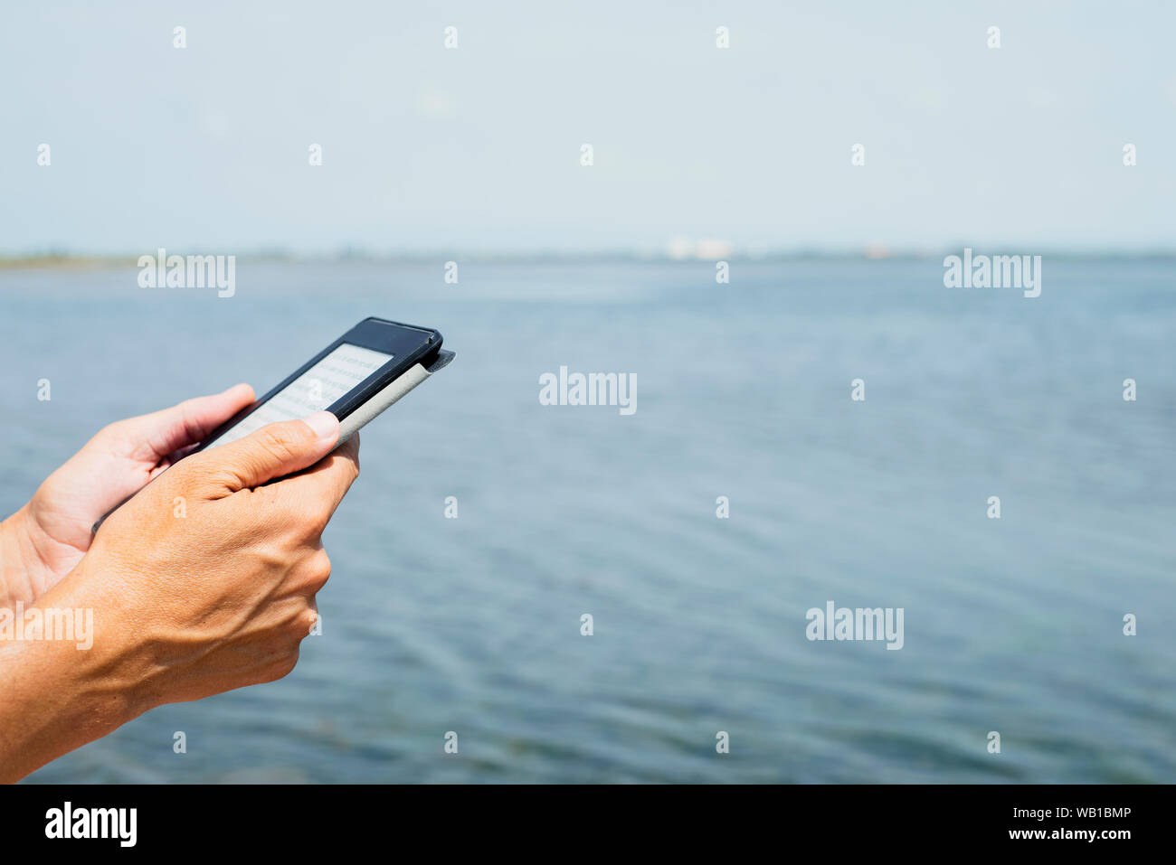 Primo piano di un giovane uomo caucasico all'aperto la lettura in un tablet PC o un e-reader accanto all'acqua Foto Stock