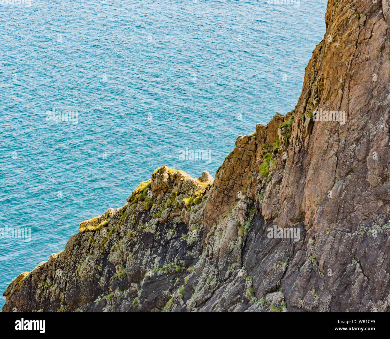 Le scogliere su delle Ebridi isola di Lewis con la luce del sole di colore cattura i licheni e muschi contro un mare blu Foto Stock