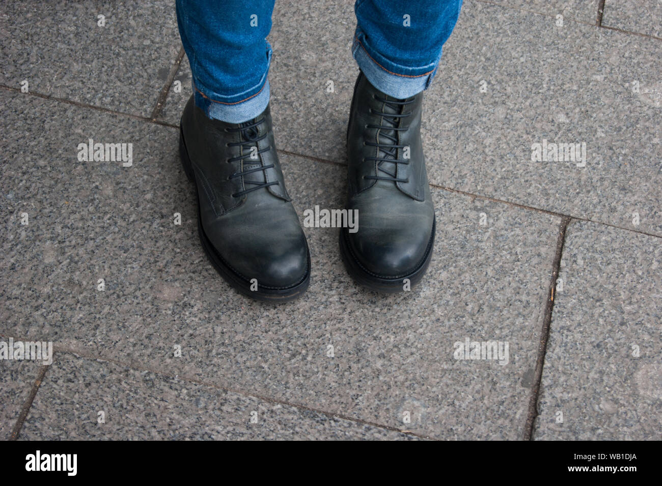 Foto di una parte del corpo umano. Gambe di Donne in nero unisex stivali e jeans stand con i calzini all'interno. Viaggiare, comfort e convenienza. Dubbi, modestia, Foto Stock