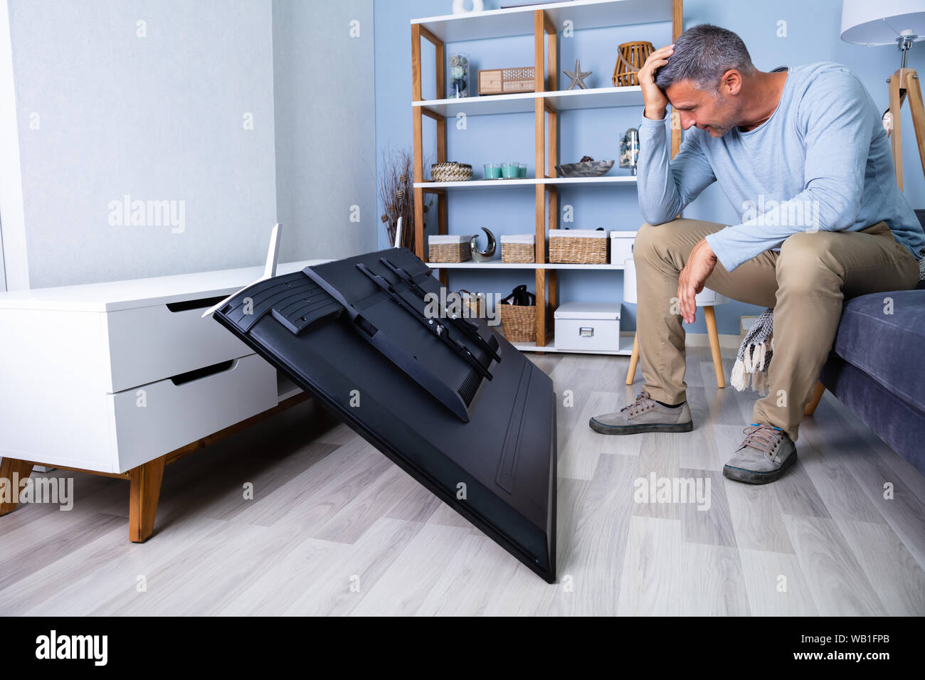 Uomo seduto sul divano davanti caduti televisione con schermo rotto Foto Stock