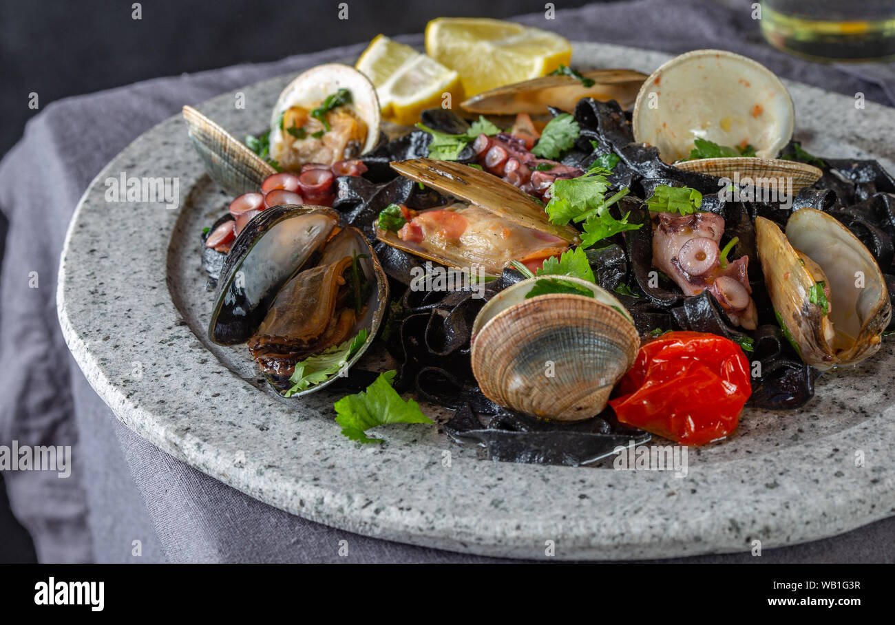 Frutti di mare fettuccine nero fehttuchini. Pasta di colore nero con calamari, polpi vongole, cozze sulla lastra di pietra. Piatto Gourmet Foto Stock
