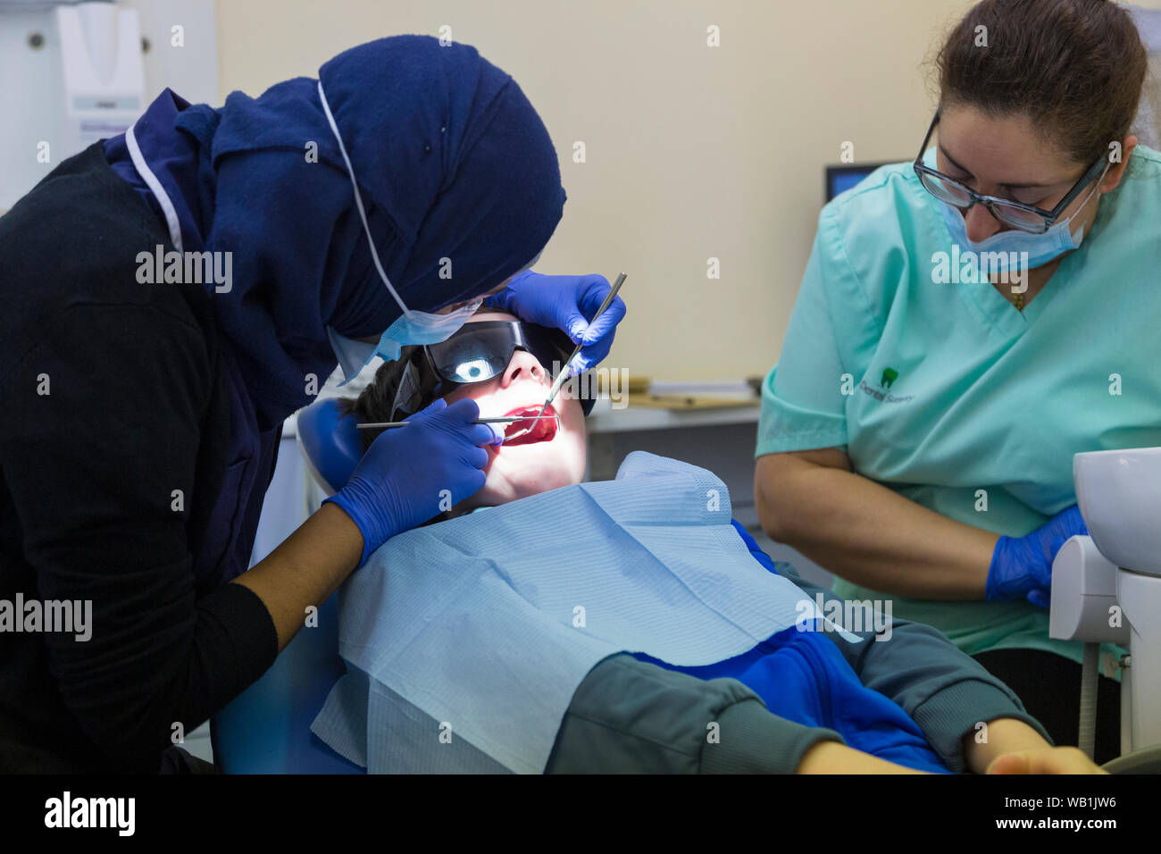 Chirurgo dentale con hijab che ispeziona i denti dei ragazzi di 13 anni con la bocca aperta durante un intervento odontoiatrico, segale, dentista, regno unito Foto Stock