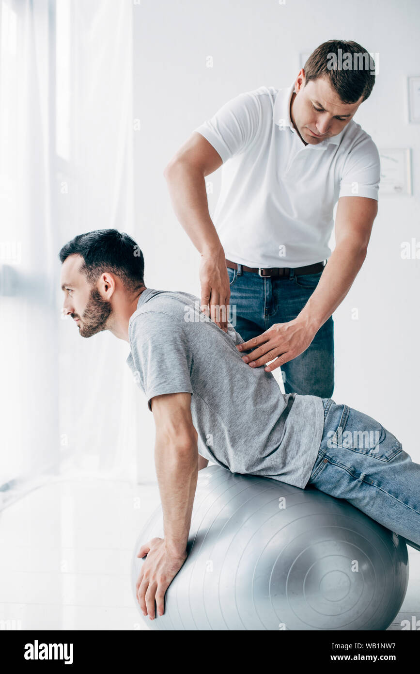 Massaggio chiropratico retro dell uomo bello giacente sulla sfera di fitness Foto Stock