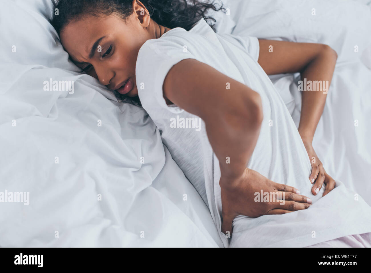 Esaurito americano africano donna che soffre di dolori alla schiena mentre giaceva sul letto Foto Stock