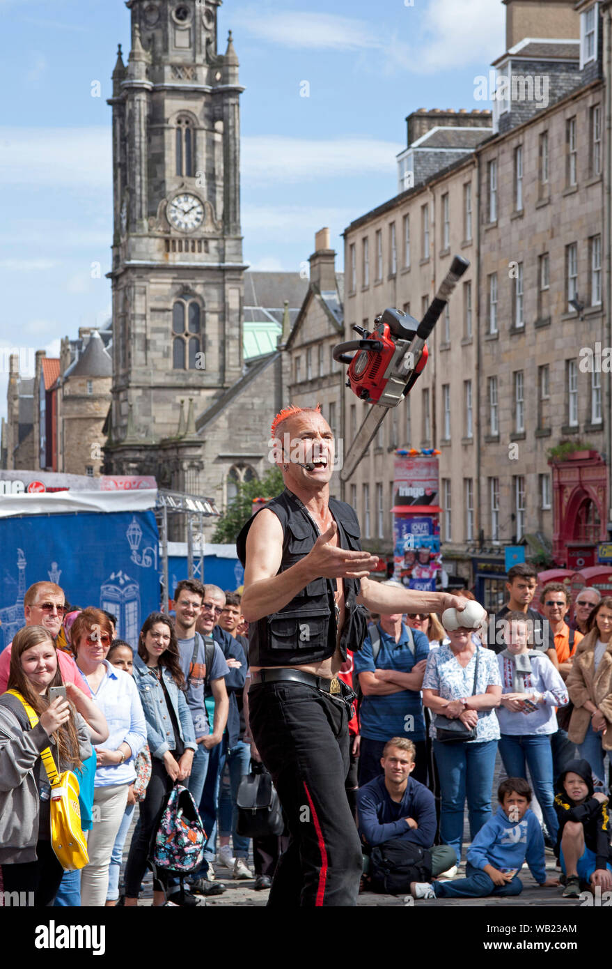 Il Royal Mile di Edimburgo, Scozia, Regno Unito. Il 23 agosto 2019. Il possente Gareth nel suo trentaduesimo anno presso la frangia intrattiene il pubblico con la giocoleria una sega a catena, con la Tron Kirk in background. Foto Stock