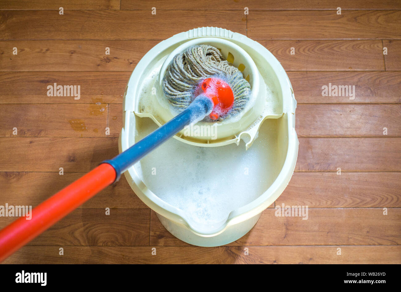 Overhead POV shot di uno spazzolone che vengono schiacciati in un secchio di pulire con acqua saponata, pronto per l'uso su un pianale interno. Foto Stock
