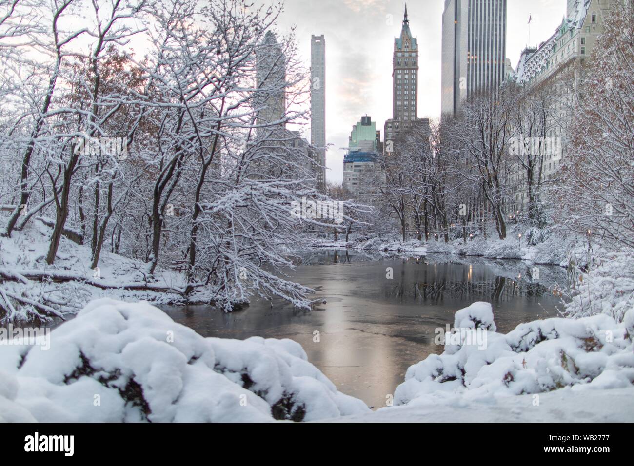 un lago ghiacciato circondato da alberi pieni di neve vicino Grattacieli di Central Park a New York Foto Stock
