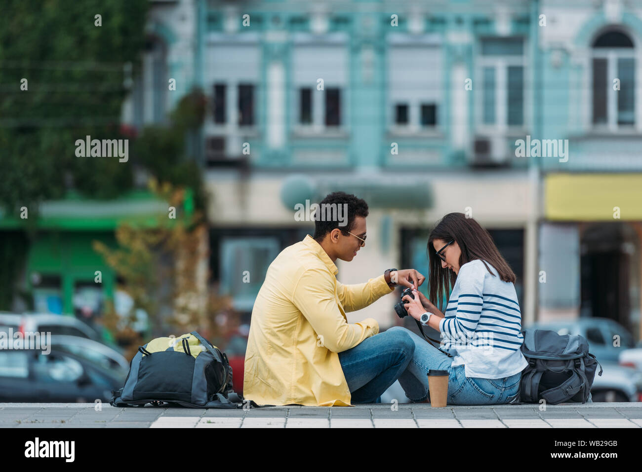 Interracial amici con zaini seduti sulle scale e impostazione telecamera Foto Stock