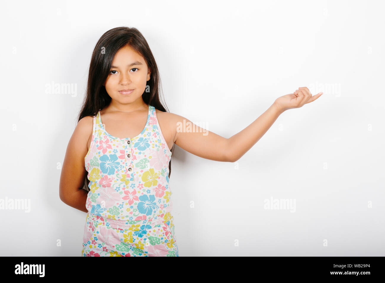 A 9 anno vecchia ragazza sta puntando al suo lato sinistro. Lei è in piedi di fronte ad una parete bianca. Ha una posizione neutra di espressione. Lei ha lunghi capelli scuri e hisp Foto Stock